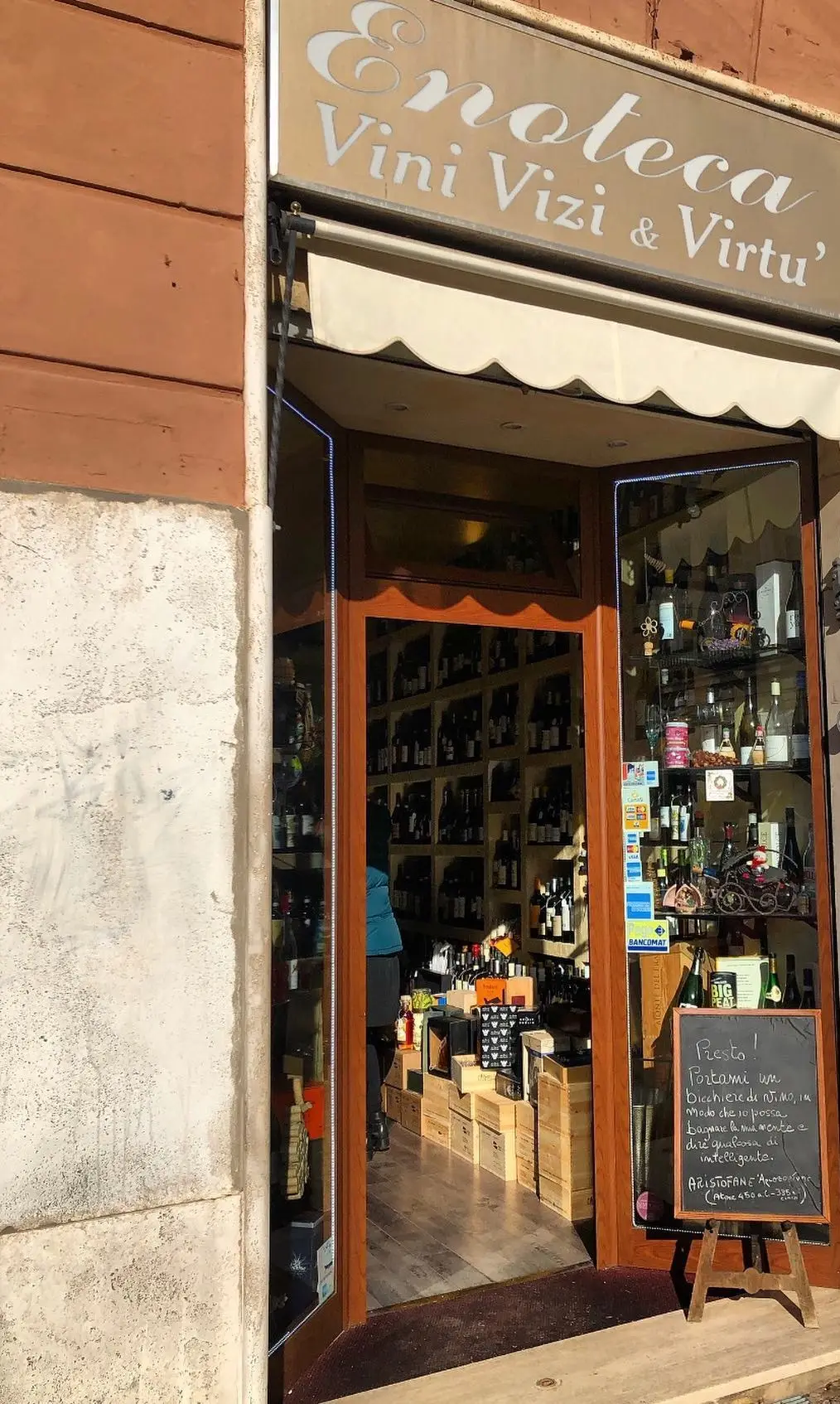 L’ingresso dell’enoteca in Piazza dell’Unità 15: l’insegna Enoteca Vini Vizi & Virtù, la tenda e la lavagna con Aristofane