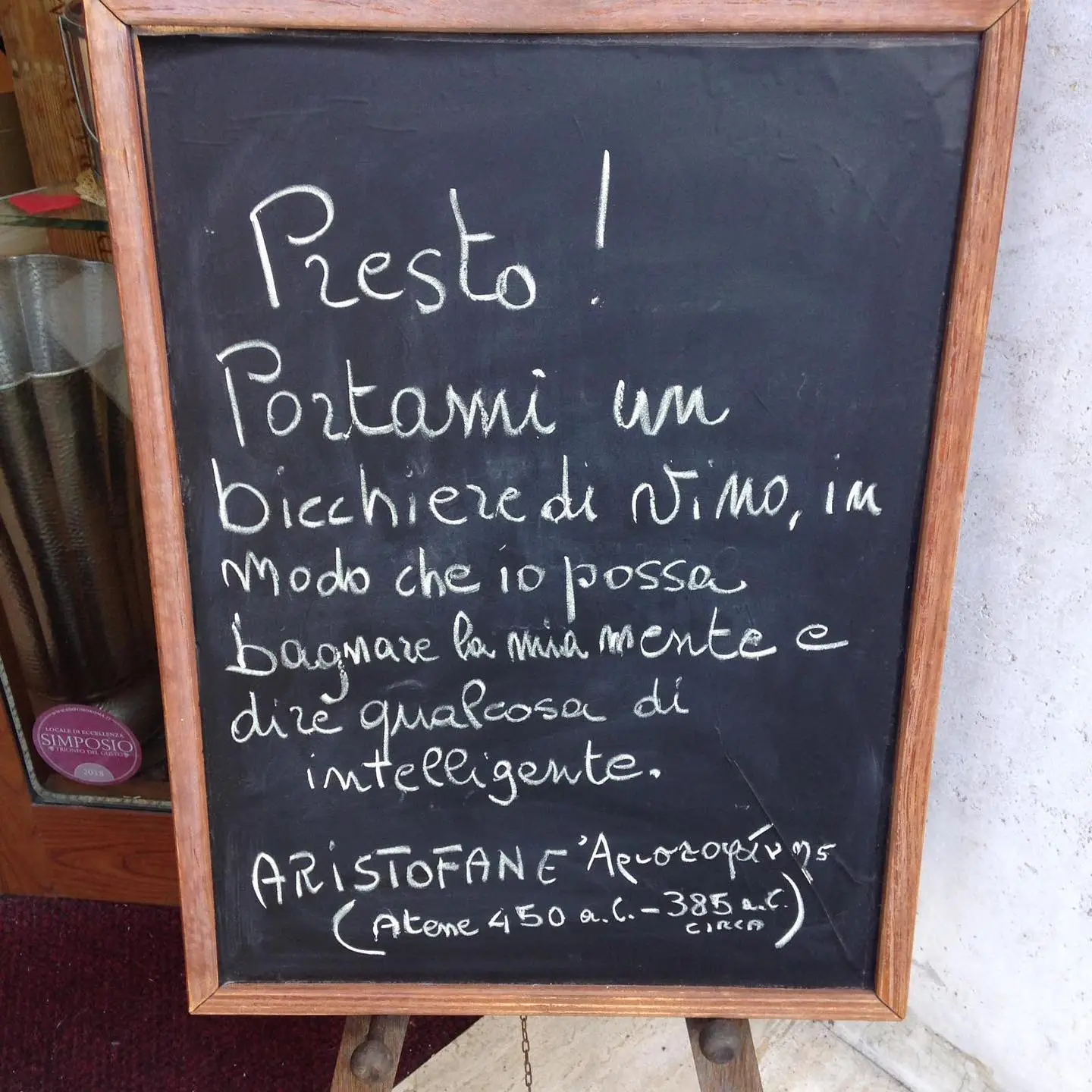 La lavagna dell’enoteca con la citazione di Aristofane scritta col gesso